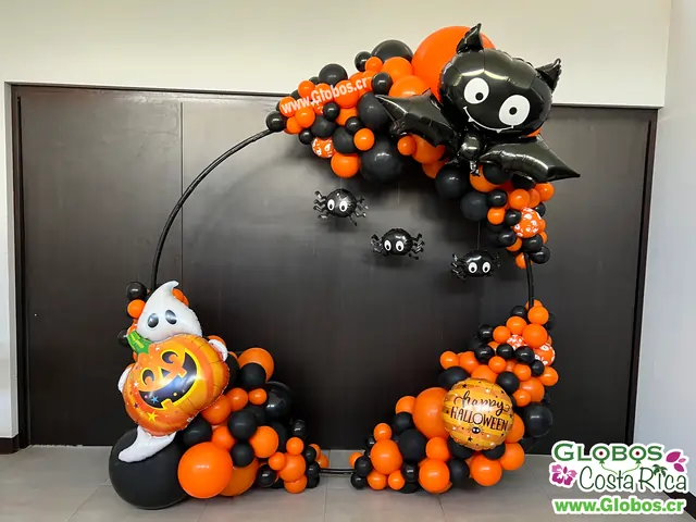 Decoración de Halloween con arco orgánico en tonos naranjas y negros con globos temáticos de murciélago y fantasma.