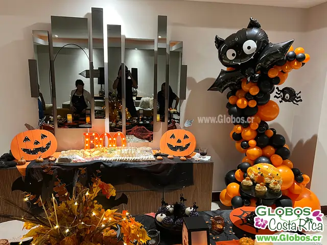 Espacio para Halloween decorado con una gran figura de murciélago hecha de globos en tonos naranjas y negros.