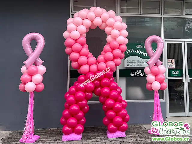 Decoración de globos en forma de lazo rosa para apoyar la concienciación del cáncer de mama frente a una clínica.